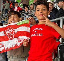 Foto: 2 Schüler halten eine Fortuna Flagge und freuen sich über ein Tor. 