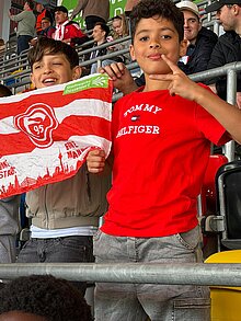 Foto: 2 Schüler halten eine Fortuna Flagge und freuen sich über ein Tor. 