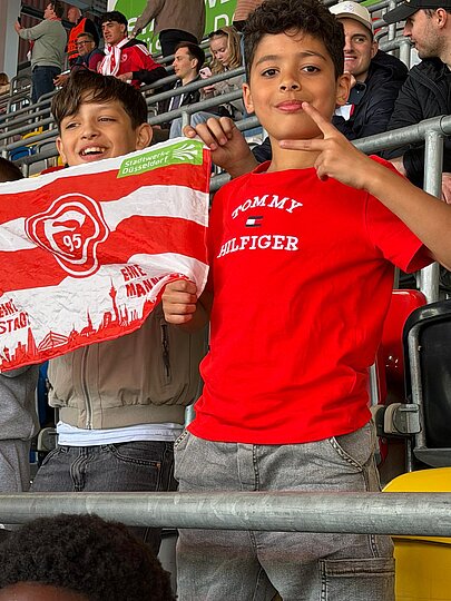 Foto: 2 Schüler halten eine Fortuna Flagge und freuen sich über ein Tor. 