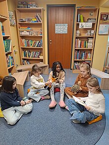 Foto Ein Kind liest vor, die anderen Kinder hören zu. 