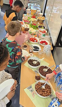 Foto Kinder stellen sich an beim Frühstücksbuffet in den Ferien der OGS. 